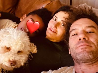 Walker Nathaniel Diggs, Idina Menzel, Aaron Lohr, and pet dog are all relaxing on the couch and Walker's face is covered with heart emoji.
